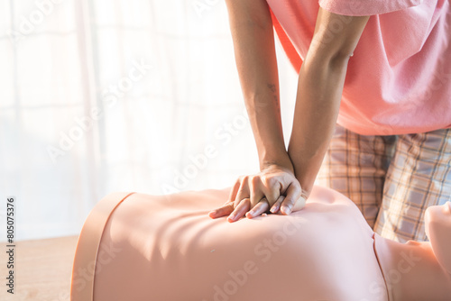 Close-up of young Asian female hands performing cardiopulmonary resuscitation (CPR) on a training dummy. Key elements include defibrillator, compressions, mouth-to-mouth, and abdominal thrusts. photo