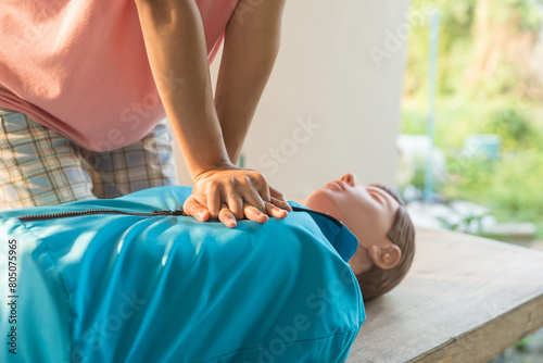 Close-up of young Asian female hands performing cardiopulmonary resuscitation (CPR) on a training dummy. Key elements include defibrillator, compressions, mouth-to-mouth, and abdominal thrusts. photo