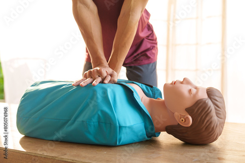 Close-up of middle-aged Asian male hands performing cardiopulmonary resuscitation (CPR) on a training dummy. Vital techniques include defibrillation, chest compressions, and maintaining the airway. photo