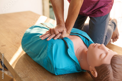 Close-up of middle-aged Asian male hands performing cardiopulmonary resuscitation (CPR) on a training dummy. Vital techniques include defibrillation, chest compressions, and maintaining the airway. photo