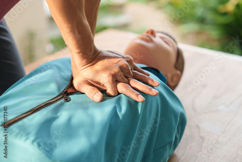 Close-up of middle-aged Asian male hands performing cardiopulmonary resuscitation (CPR) on a training dummy. Vital techniques include defibrillation, chest compressions, and maintaining the airway. photo