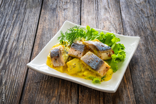 Marinated herring fillets in mustard sauce with dill and lettuce on wooden table
