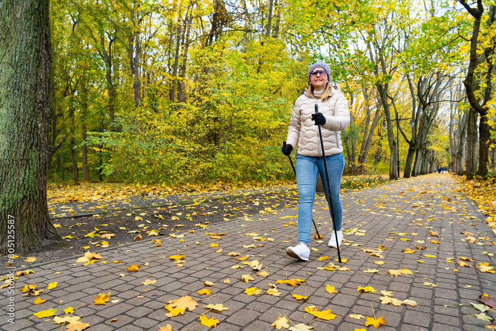 Fototapeta premium Mid-adult woman exercising Nordic walking in city park 