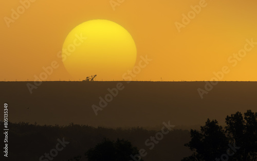 Silhouette of excavator on quarry dump with sunset in background