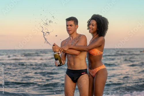 Interracial Couple Popping Champagne on Beach - Romantic Sunset Celebration © Lomb