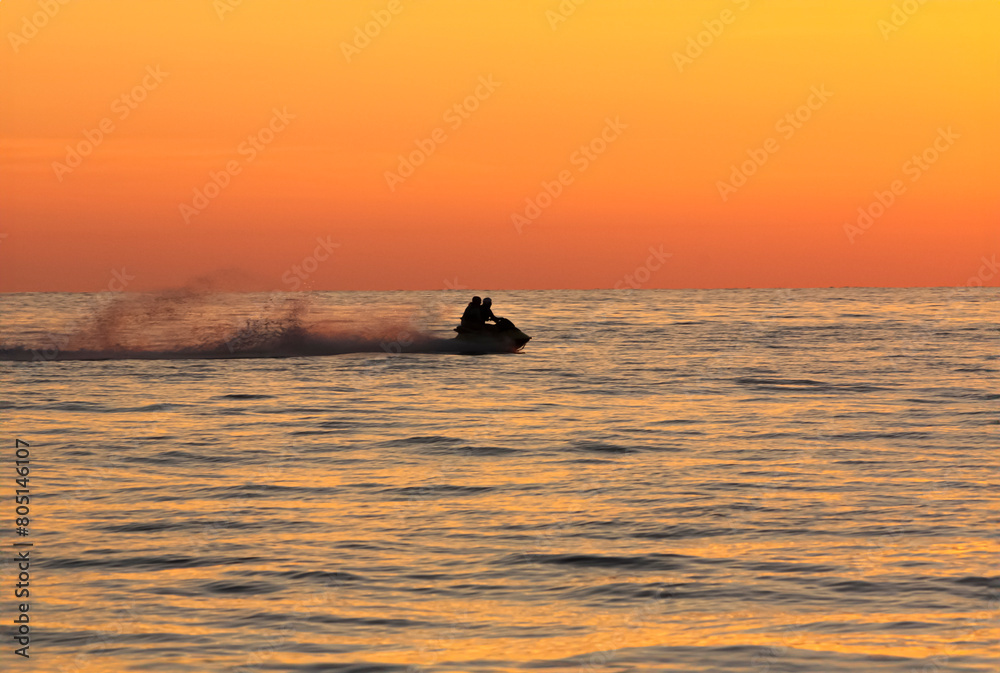 Sunset silhouette of a couple on a jet-ski in the sea