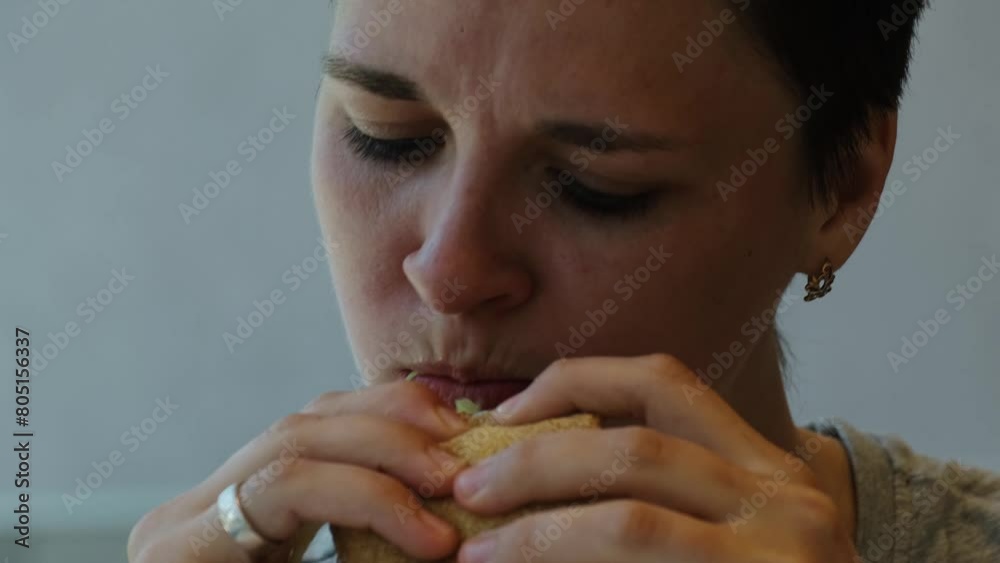 Close up young pretty woman with short haircut eating hamburger sitting in fast food cafe. Girl enjoys biting into a burger with chicken cutlet, vegetables and bacon Close up young pretty woman with short haircut eating hamburger sitting in fast food cafe. Girl enjoys biting into a burger with chicken cutlet, vegetables and bacon