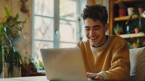 Young man using laptop and smiling at home. Man sitting by table working on laptop computer