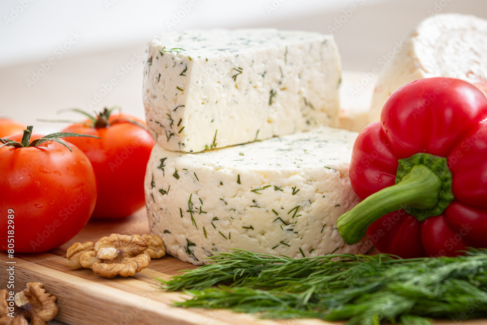 Cut cheese heads on wooden board served with tomatoes and fresh paprica and herbs, olive oil, olives and bread. Serving French homemade cheese. Food concept Cut cheese heads on wooden board served with tomatoes and fresh paprica and herbs, olive oil, olives and bread. Serving French homemade cheese. Food concept