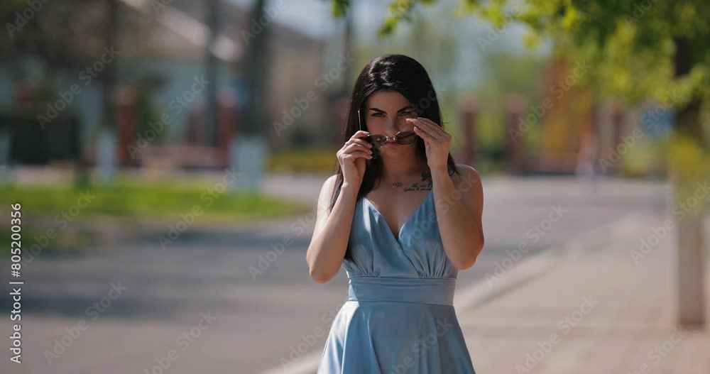 Attractive brunette lady in blue dress wearing sunglasses walking at summer city, slow motion Attractive brunette lady in blue dress wearing sunglasses walking at summer city, slow motion