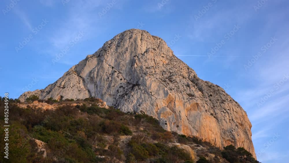View of Peñón de Ifach mountain. Beautiful warm colours reflecting on the mountain peak at sunset. Natural Park in Calpe city, Alicante Province, Spain. Famous travel attraction, can be visited daily. View of Peñón de Ifach mountain. Beautiful warm colours reflecting on the mountain peak at sunset. Natural Park in Calpe city, Alicante Province, Spain. Famous travel attraction, can be visited daily.