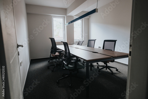 A well-lit modern office conference room featuring a long table, ergonomic chairs, and a contemporary lighting fixture, ideal for business meetings.