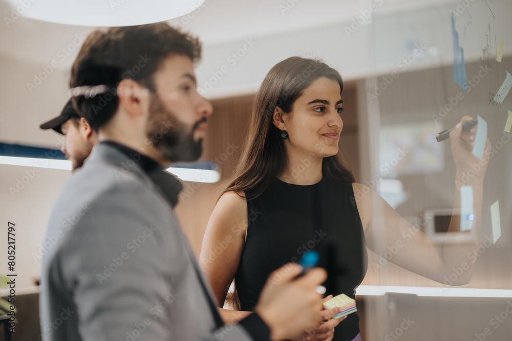 An engaged business team is seen brainstorming ideas on a glass wall using sticky notes, discussing growth and results in a contemporary office space. An engaged business team is seen brainstorming ideas on a glass wall using sticky notes, discussing growth and results in a contemporary office space.