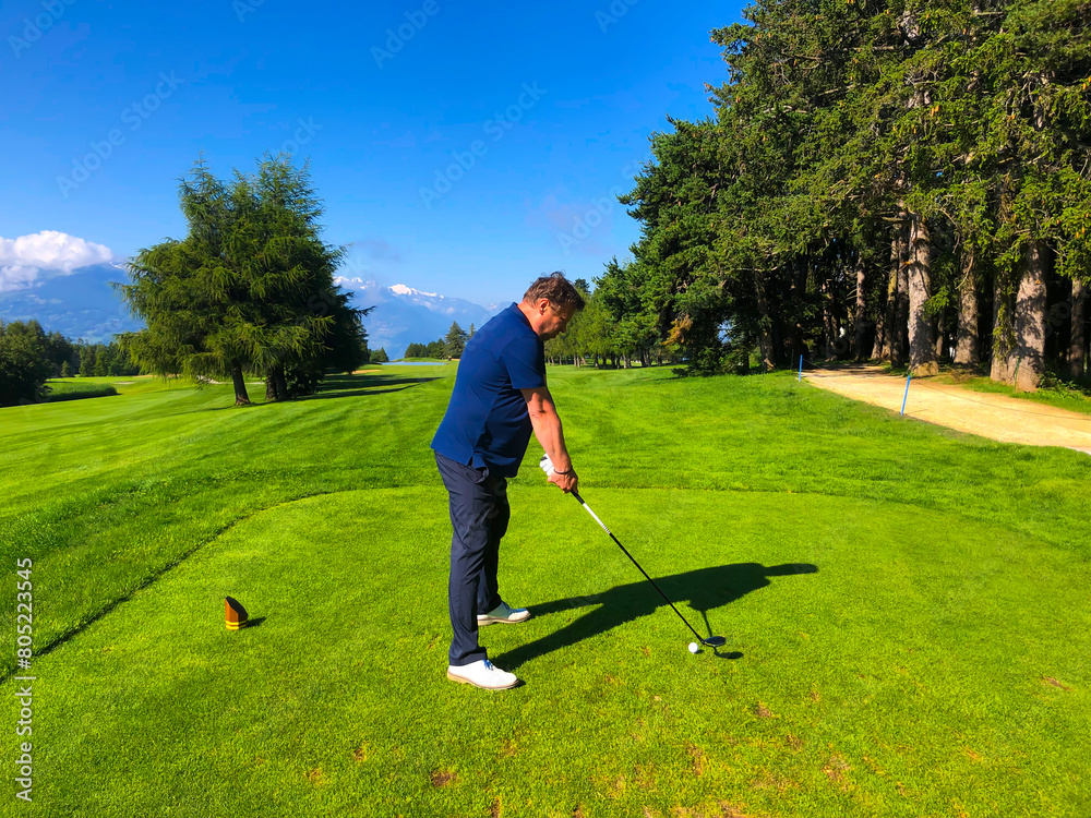 Golfer Teeing Off on Golf Course with Mountain View in Crans Montana in Valais, Switzerland. Golfer Teeing Off on Golf Course with Mountain View in Crans Montana in Valais, Switzerland.