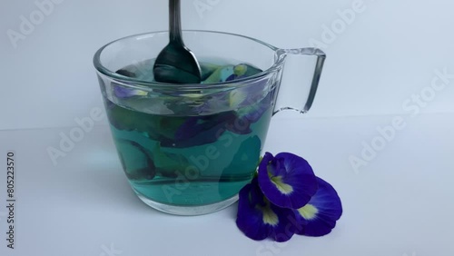 Spoon stiring of  butterfly pea flower tea, or Clitoria ternatea. Inside transparent glass, isolated on white background. Time lapse diffusion  photo