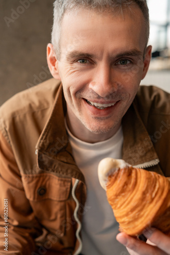 Close-up of a smiling man sitting in a cafe eating a croissant dipped in a frothy hot drink