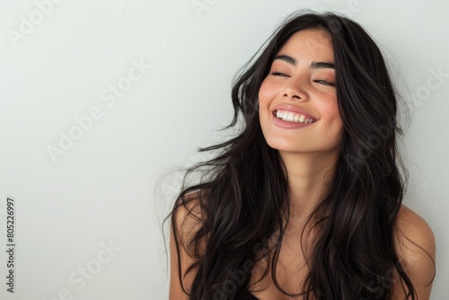Carefree and happy woman with long dark hair laughing against a plain background
