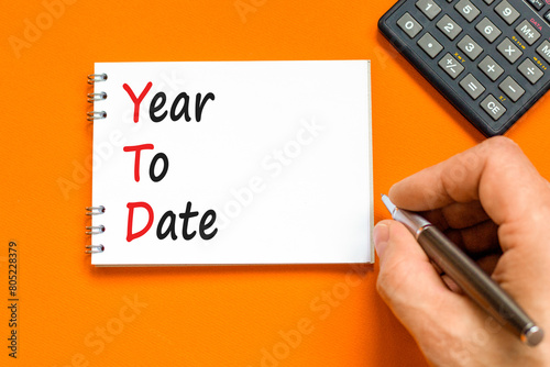 YTD year to date symbol. Concept words YTD year to date on beautiful white note. Beautiful orange background. Businessman hand. Business YTD year to date concept. Copy space. photo