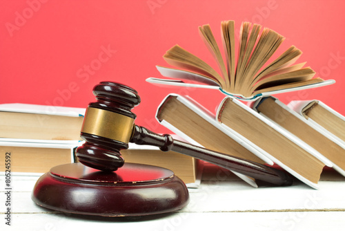Law concept - Open law book, Judge's gavel, scales, Themis statue on table in a courtroom or law enforcement office. Wooden table, red background.