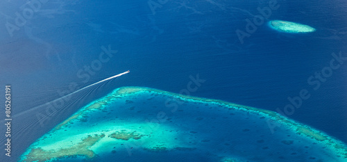 Maldives islands beach with speed boat passing from birds eye view. Aerial view on Maldives island Ari atoll. Tropical islands and atolls from aerial view. Summer tourism background. Wanderlust travel photo