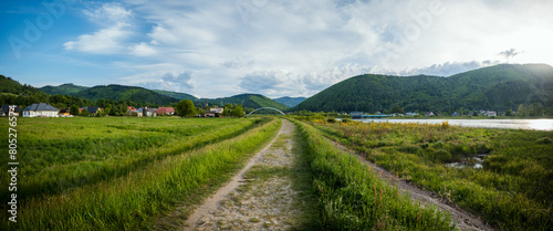 Panorama of the village of Porąbka seen from the walking path along Lake Czanieckie. Spring in the Beskid Mały Mountains. The bridge in the distance. A fragment of the blue tourist trail