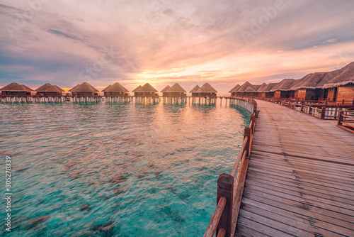 Fototapeta Naklejka Na Ścianę i Meble -  Perfect sunset on Maldives island, luxury water villas resort and wooden pier. Beautiful cloudy sky and beach background for summer vacation tourism travel vibes. Pristine sea water corals calm waves.
