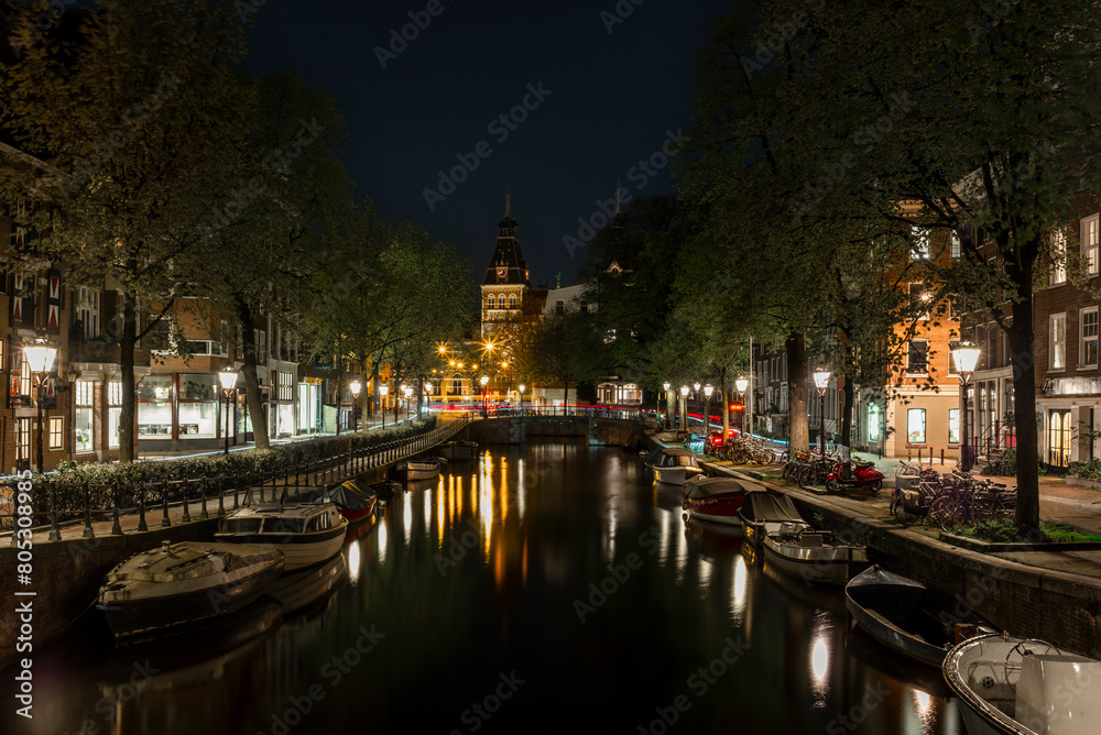 Boats and reflection of the Rijksmuseum on the Spiegelgracht canal in Amsterdam at night with cars light trails