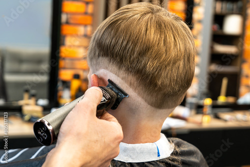 Shooting in a beauty salon. A barber cuts the hair of a little boy with a machine.