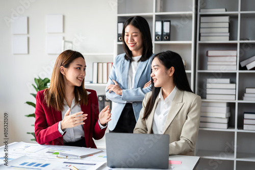 Three women are sitting at a desk with a laptop in front of them