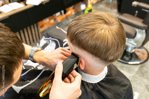 The picture of a blonde child with blue eyes and freckles is in a barbershop beauty salon. The miller holds a milling trimmer in his hand. © BUCSA
