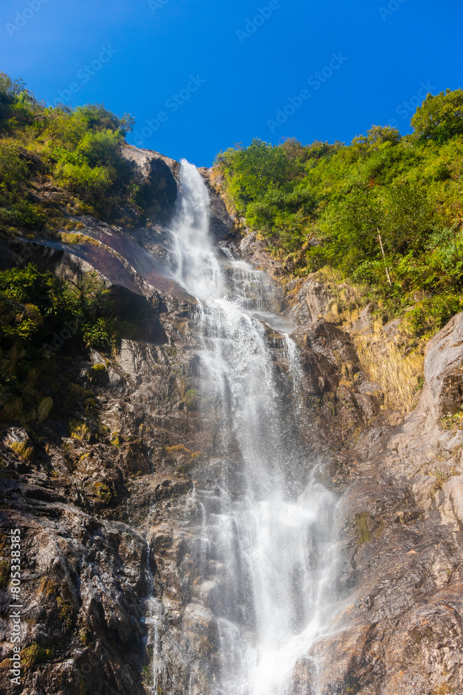 Fototapeta premium A waterfall flowing in a rocky area. The cascading water creates a beautiful natural landscape in a mountainous setting. The rushing water adds to the serene outdoor environment. Sikkim, India