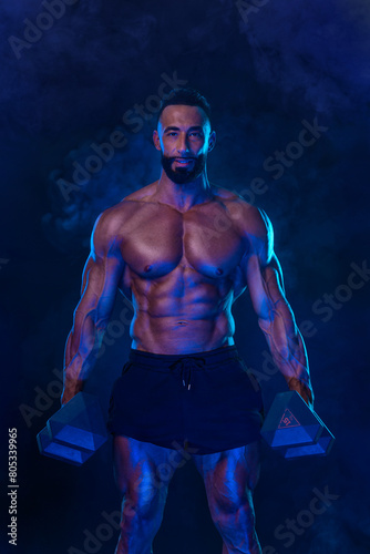Sporty fit man athlete with dumbbells make fitness exercises on neon background. Download cover for music collection for fitness classes. Sports recreation.