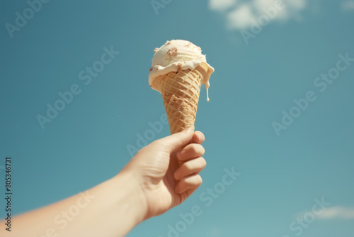 Hand holding ice cream cone against clear blue sky. High angle view photo. Summer treat and dessert concept. Design for poster, banner, invitation