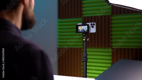 a young man film video of himself on the phone and displays the video on the monitor screen