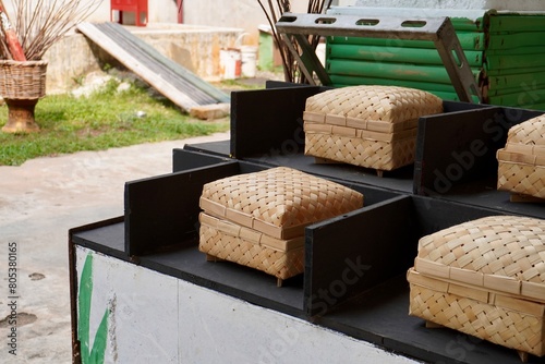 Indonesian styled rattan bamboo anyaman bambu organic eco friendly square box storage handmade crafts isolated on horizontal ratio black sectioned table and outdoor grasss background.