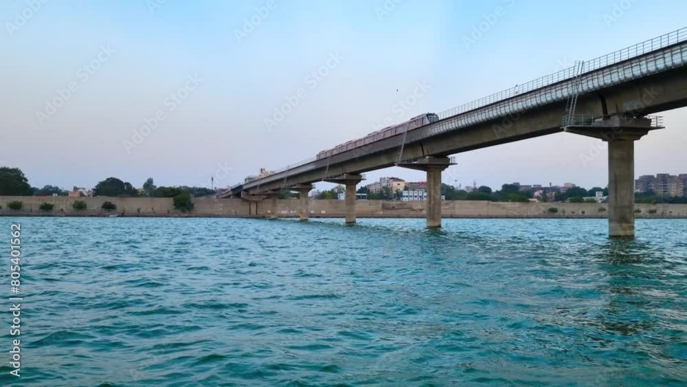 Metro rail train locomotive crossing over the blue waters of a river on an overhead bridge showing the infrastructure development in Gujarat, Ahmedabad, India Metro rail train locomotive crossing over the blue waters of a river on an overhead bridge showing the infrastructure development in Gujarat, Ahmedabad, India