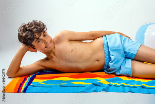 Fotografie Smiling shirtless boy wearing swim trunks and casually resting head in hand on a