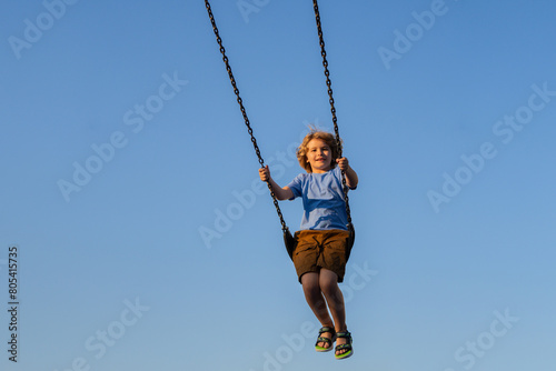 Kid swinging high. Adorable blonde child having fun on a swing on playground. Happy kid swinging on playground area. Summer playground. Child swinging high.