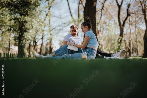 Teenage couple sitting on grass at a park, smiling and sharing a moment with books in hand
