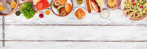 Summer BBQ or picnic top border with hamburgers, hotdogs, salad and snacks. Overhead view over a white wood banner background. Copy space.