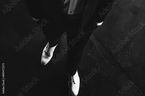 Projecting an aura of sophistication, a gentleman stands agnst a backdrop of darkness, his black attire and white shoes creating a striking visual contrast.