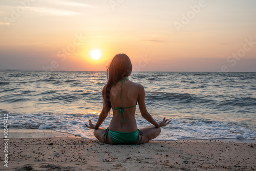 Foto Asian tourist wearing a sexy bikini, exercising, stretching, doing yoga, beautiful beach by the sea, sunset, relaxing, summer time, vacation
