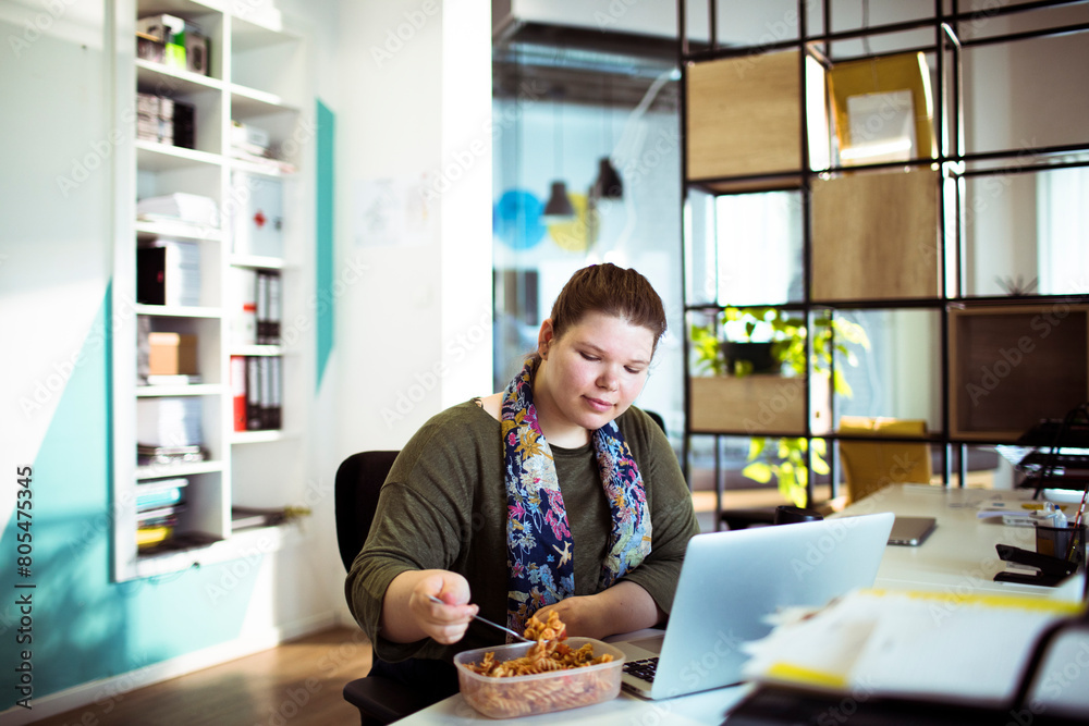 Woman enjoying lunch break at her desk in a bright office Woman enjoying lunch break at her desk in a bright office