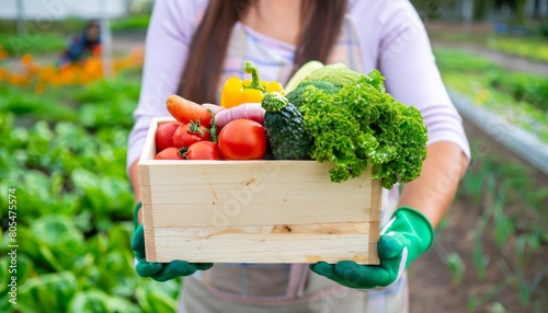 A close-up view of a woman cradling a wooden crate filled with freshly picked vegetables from the field.