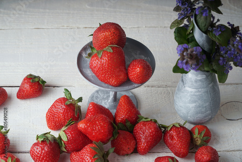 Strawberries and a vase with flowers on a wooden table. A wonderful summer picture of flowers and fresh berries
