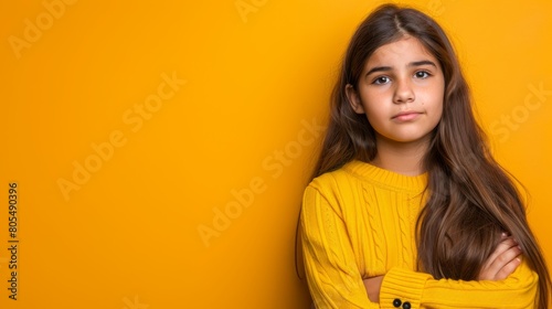  A young girl in a yellow sweater poses, crossing her arms and turning her head to the side for a photograph