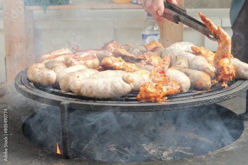 Fried sausages and chicken wings on barbecue grill in the village. Frying meat on open fire. Barbecue party on backyard of country house cabin. Street food festival. Home cooking outdoor. Picnic time