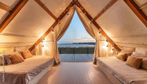 A canvas and wood A-frame glamping tent is comfortably furnished with two beds and warm glowing string lights,a beautiful lake view from the patio at an Eco resort, luxury camping photo