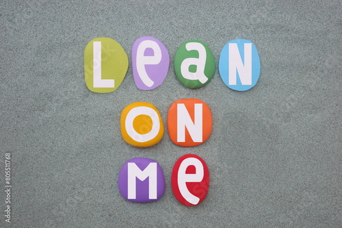 Lean on me, motivational slogan composed with hand painted multi colored stone letters over green sand