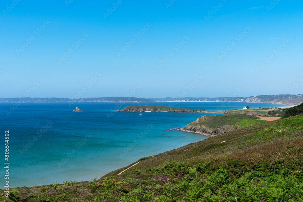 La mer d'Iroise, encerclée de falaises imposantes, étincelle sous un ciel estival d'un bleu profond, offrant un spectacle captivant sur la presqu'île de Crozon, où la nature dévoile toute sa splendeur